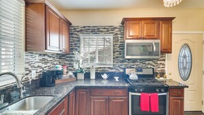 A kitchen with wooden cabinets, a microwave, a stove, and a window with blinds. - Sunny Hemet Escape w/ Covered Porch & Fire Pit (Hemet)