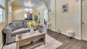 A living room with a sofa, coffee table, and a kitchen in the background. - Sunny Hemet Escape w/ Covered Porch & Fire Pit (Hemet)