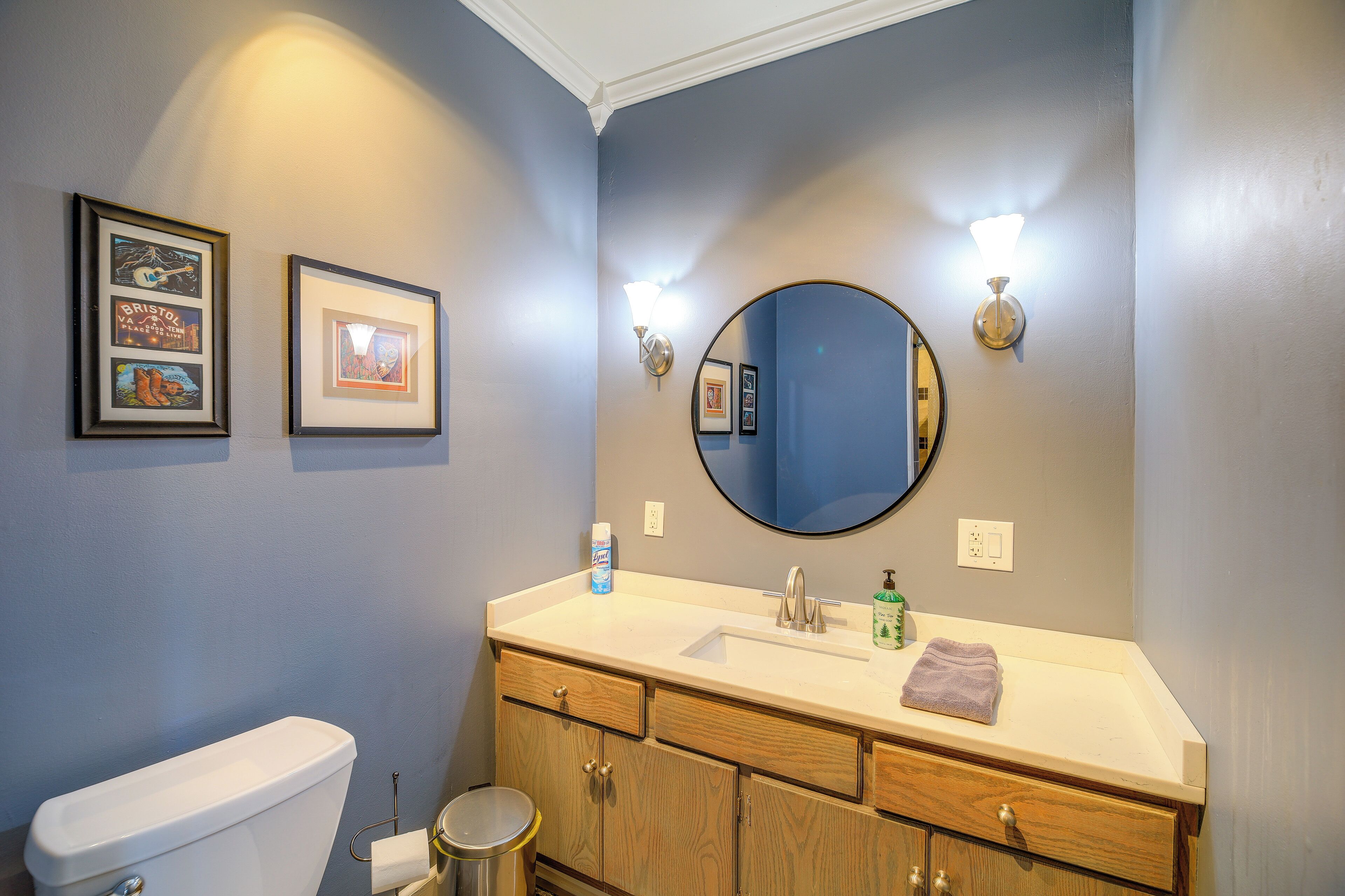 Une salle de bain comprenant des toilettes, un lavabo, un meuble-lavabo, des tableaux encadrés et un miroir.