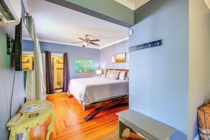 Une chambre à coucher comprenant un lit, un ventilateur de plafond, un plancher en bois, une table de chevet et une étagère fixée au mur.