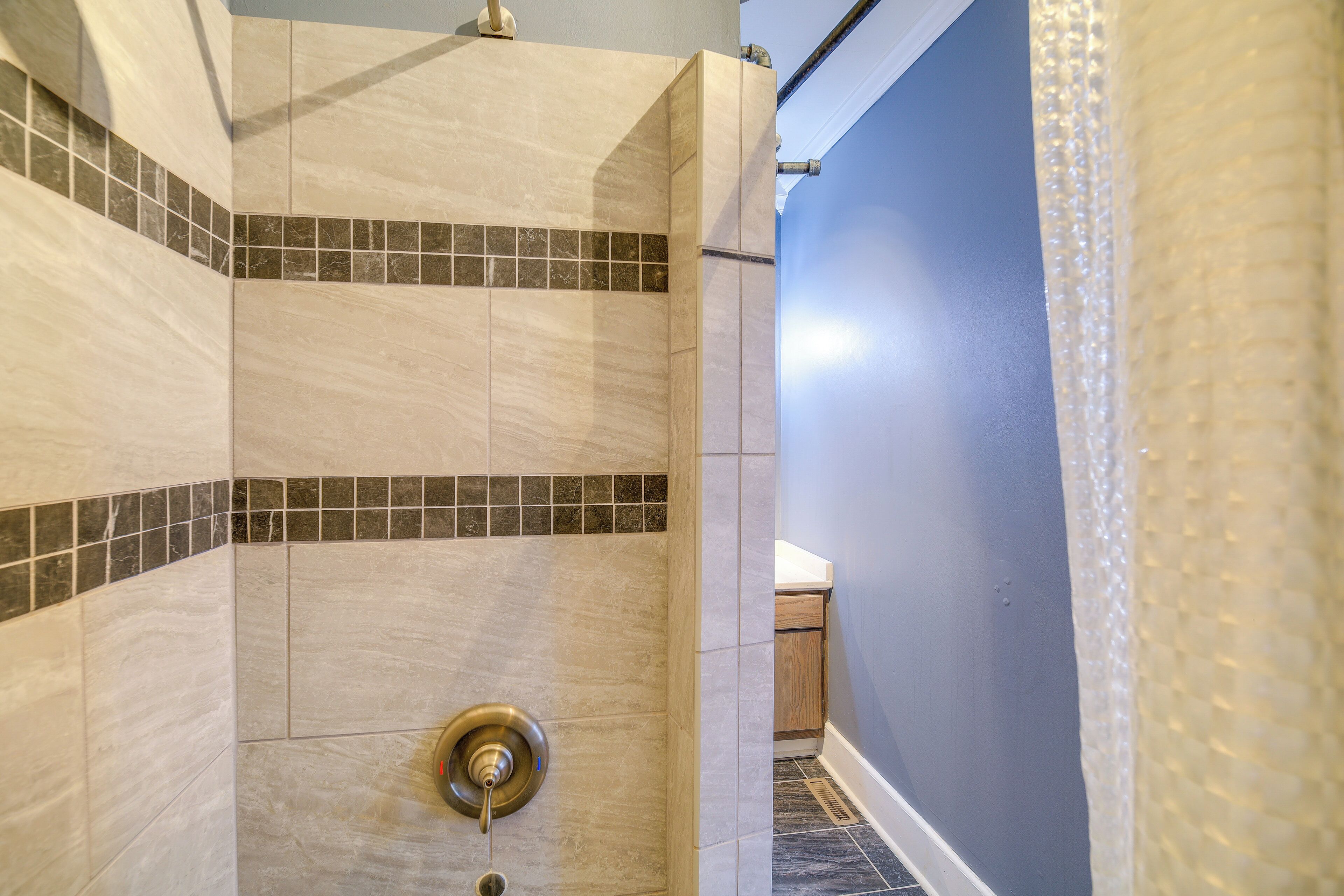 A shower with beige tiles and a small section of dark tiles at the bottom.