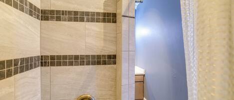 A shower with beige tiles and a small section of dark tiles at the bottom.