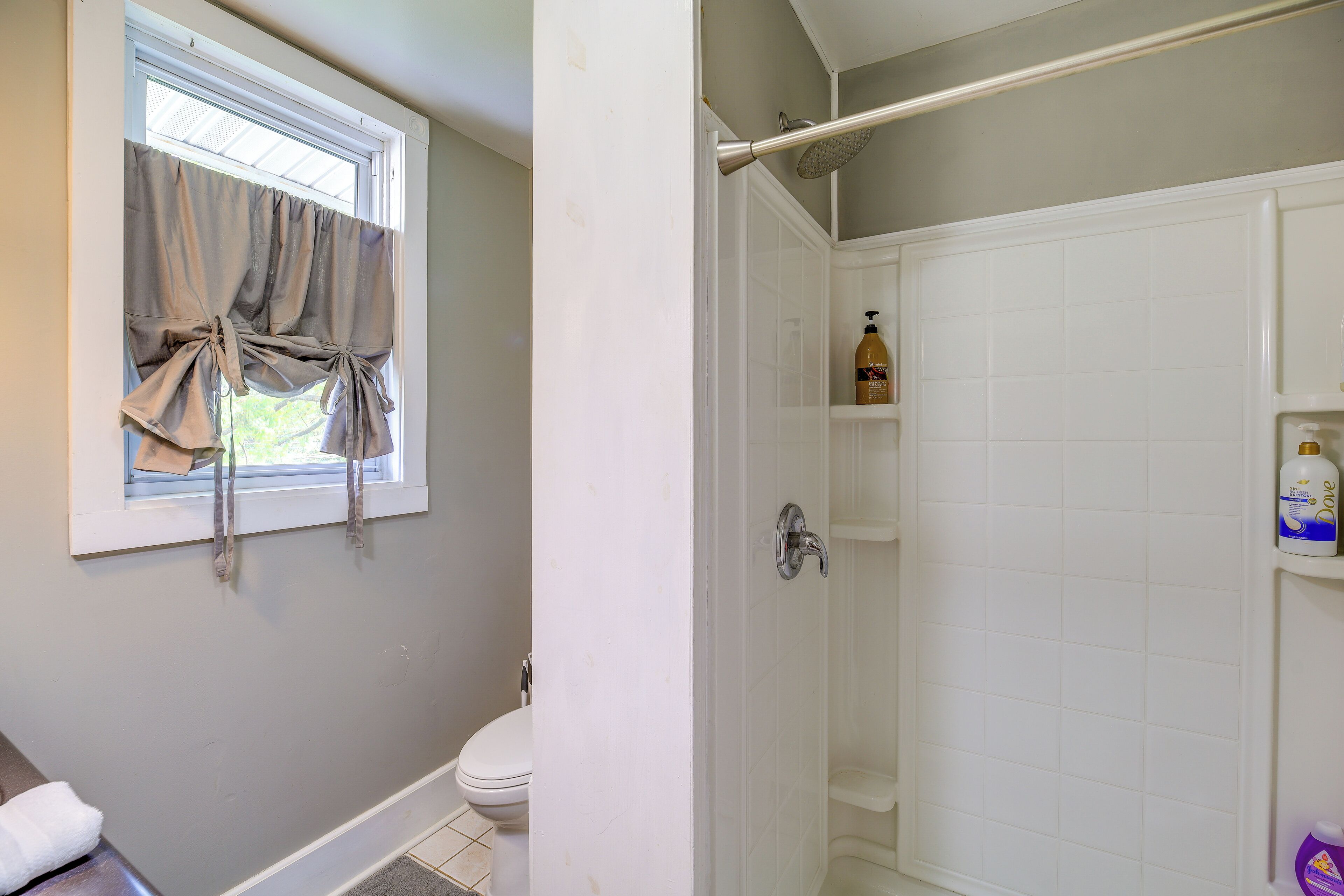 Un baño con inodoro, ducha y ventana con cortinas.