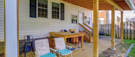 A covered patio with a wooden table and chairs, a small staircase, and a wooden fence.