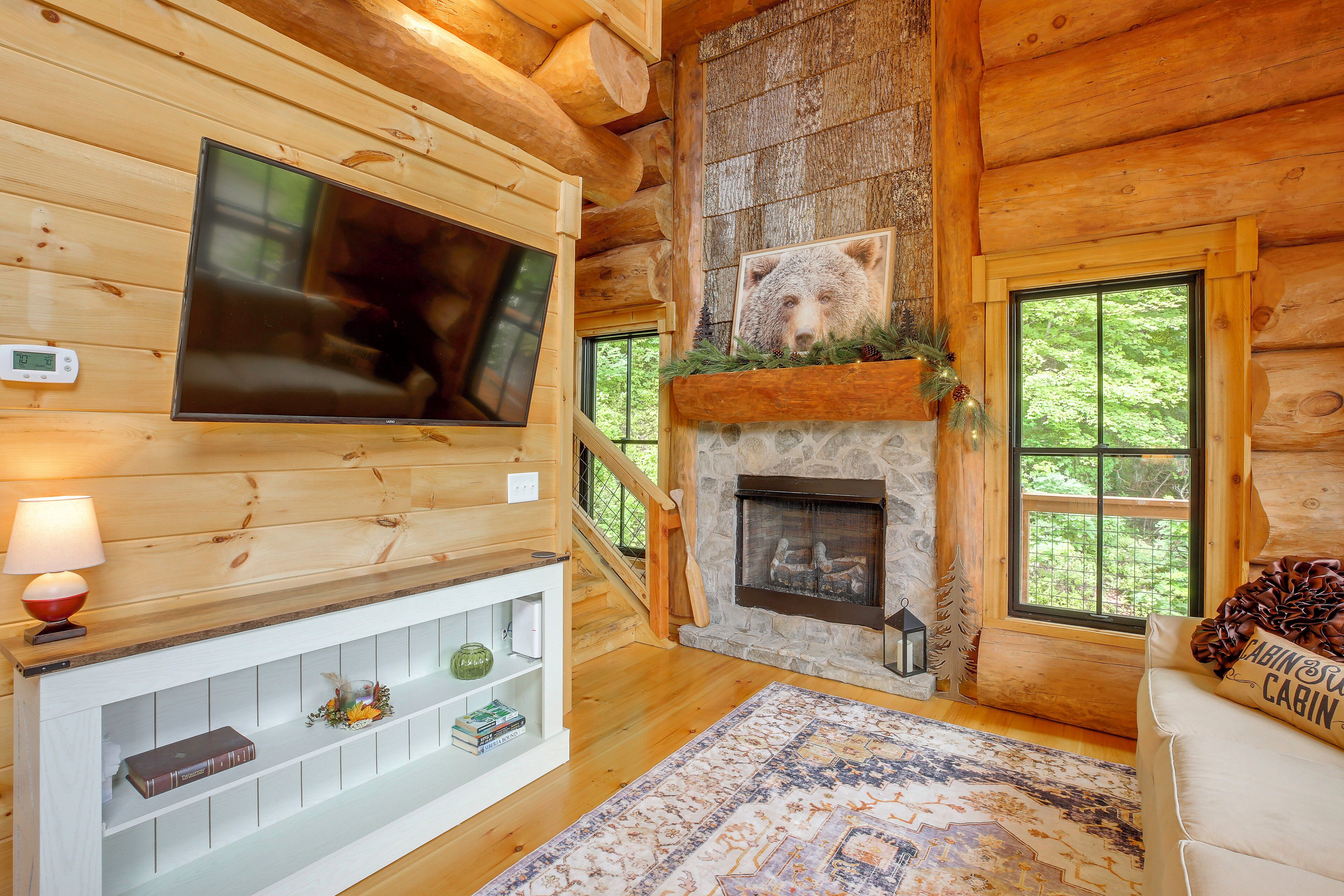 L’intérieur d’une cabane en rondins, avec une cheminée, un téléviseur fixé au mur et un coin salon confortable.