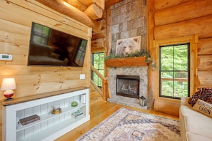 A log cabin interior with a fireplace, a mounted television, and a cozy seating area. - Fish, Float & Relax! Riverfront Retreat in Sparta (Sparta)