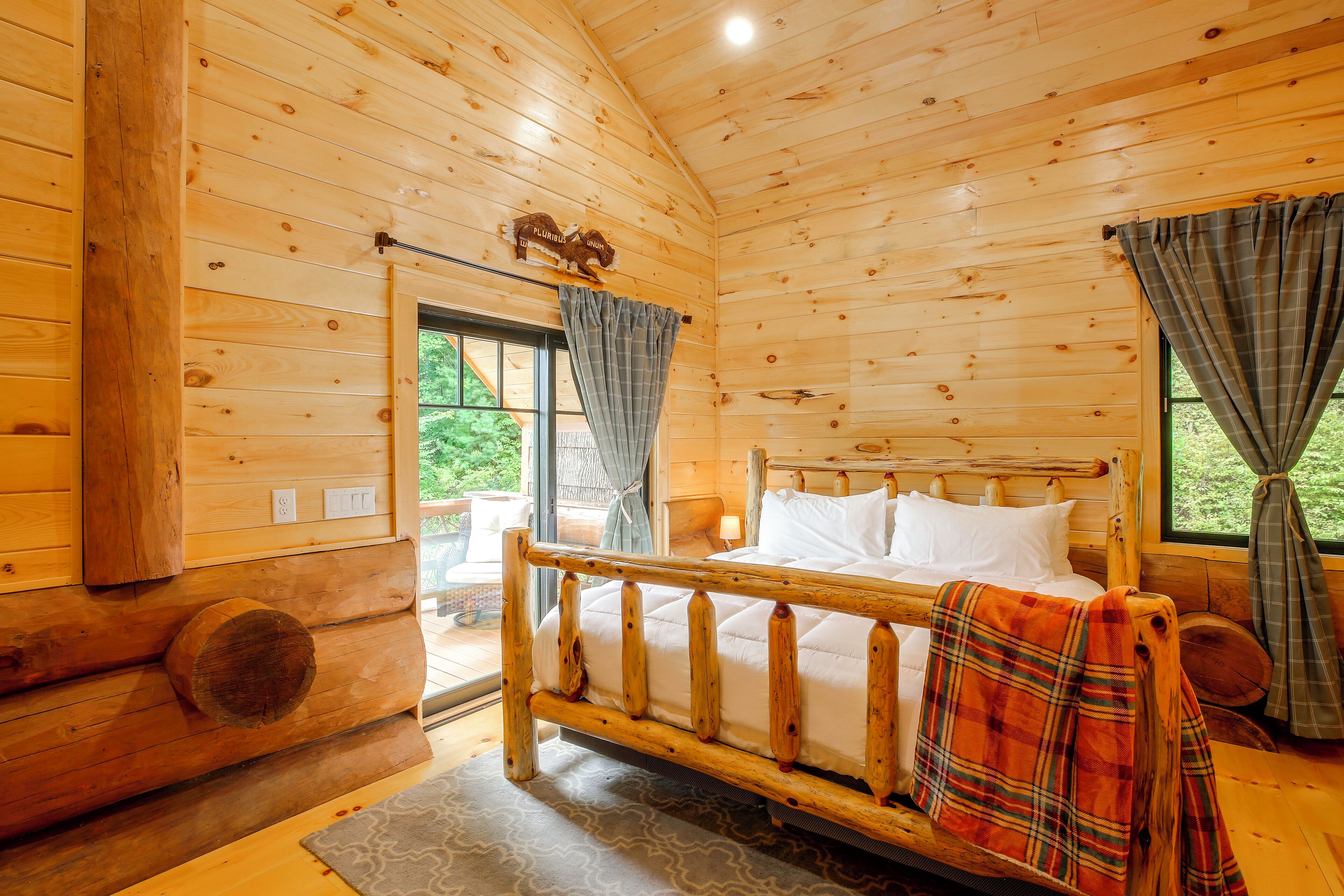 A wooden cabin room with a bed, a window, and a view of greenery outside.