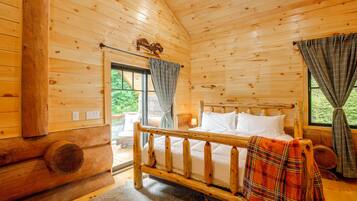 A wooden cabin room with a bed, a window, and a view of greenery outside.