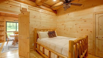 A wooden cabin interior with a bed, a dining table, and a ceiling fan.