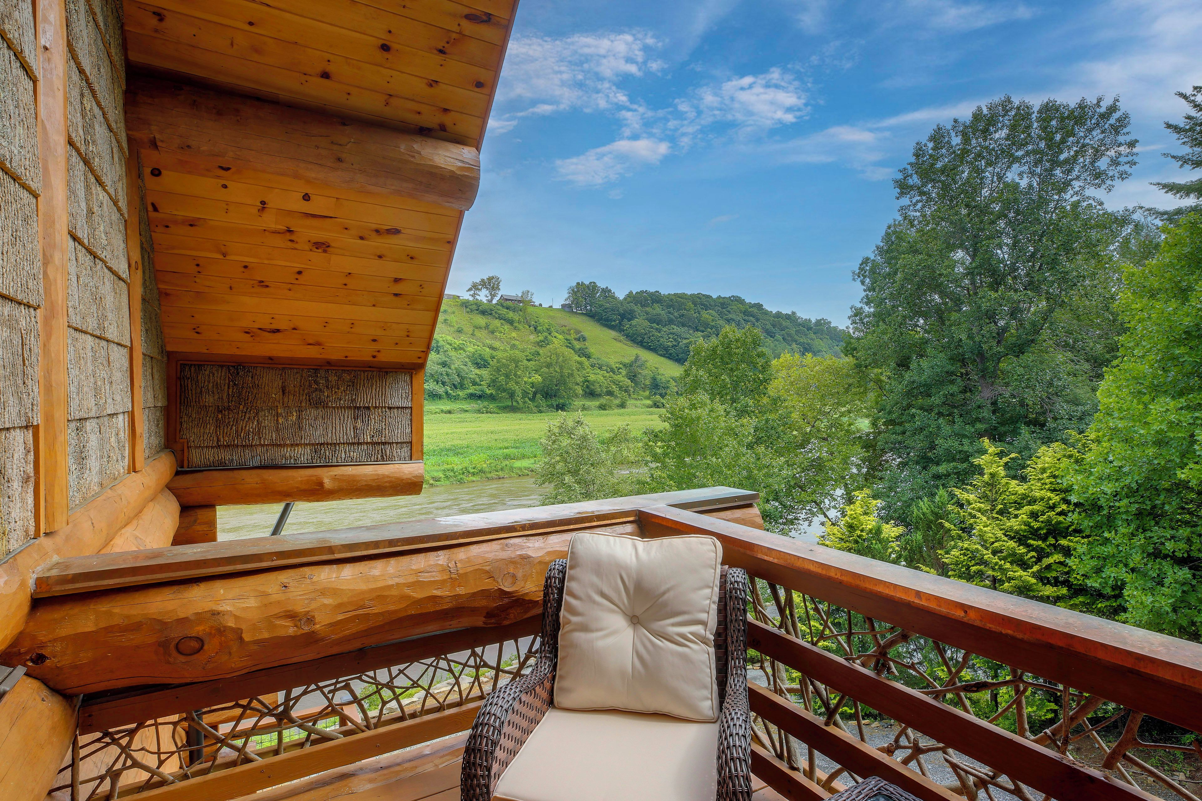 Un balcón de madera con una silla de mimbre y vista a un río y colinas.