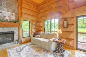 Ein Blockhaus-Interieur mit Kamin, einer Couch, einer Lampe und Blick ins Freie.