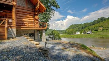 A log cabin with a stone foundation, a wooden deck, and a river view.