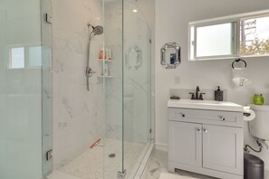 Ein modernes Badezimmer mit einer einachig gefliesten Dusche, einem weißen Waschtisch mit Spiegel und einem Fenster über dem Waschbecken.