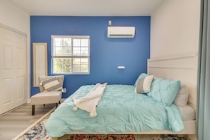 Ein Schlafzimmer mit Bett, Sessel, Fenster und Klimaanlage.
