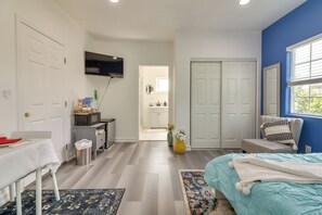 Un dormitorio con cama, escritorio, televisor y baño visible a través de una puerta abierta.