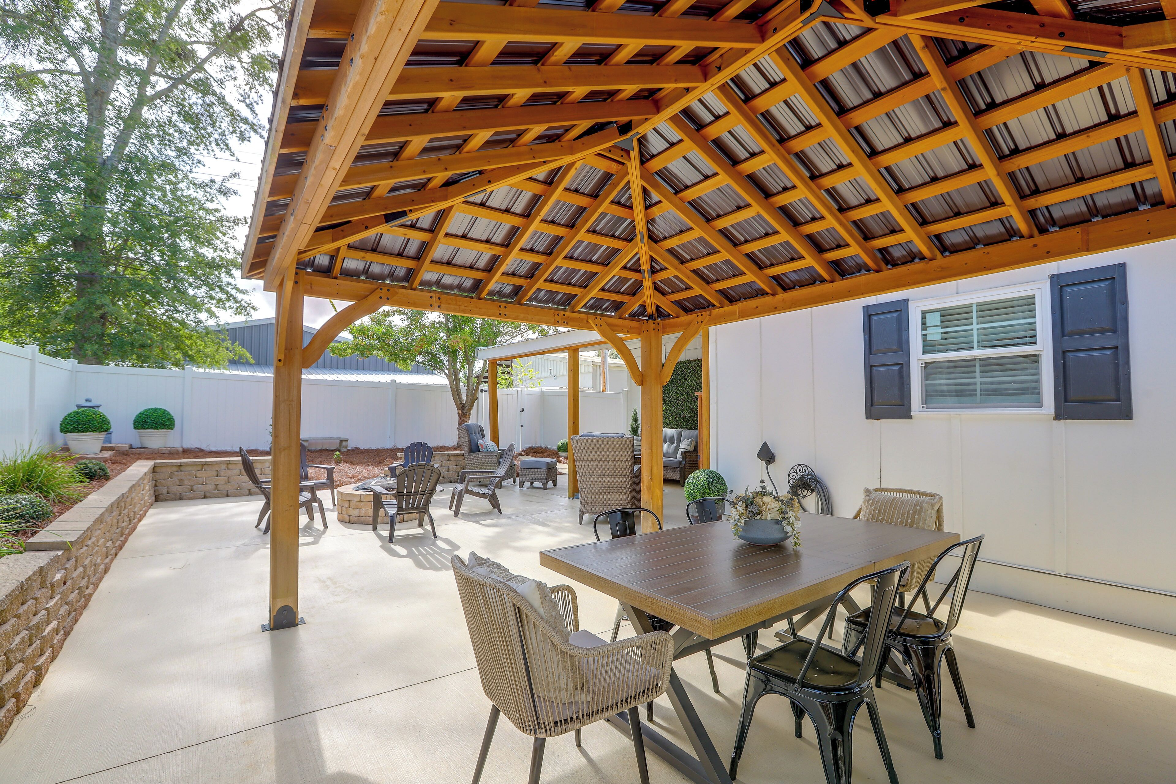 An outdoor patio with a wooden pergola, seating area, and a dining table.