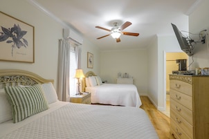 Un dormitorio con dos camas, un ventilador de techo, una mesita de noche con lámpara, un aparador y un televisor montado en la pared.