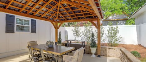 A covered patio area with a wooden pergola, a dining table with chairs, and potted plants.