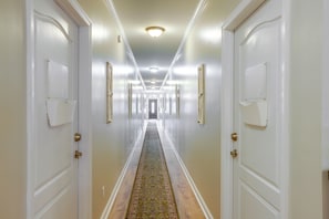 Un pasillo de hotel con puertas blancas, alfombra estampada y una lámpara en el techo.