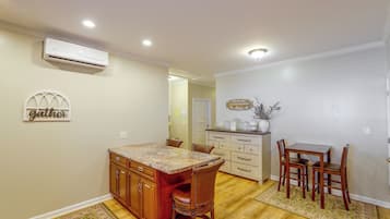 A kitchen with a dining area, wooden cabinets, a marble countertop, and a wall-mounted air conditioner.