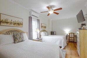 A hotel room with two beds, a ceiling fan, a television, and artwork on the walls.