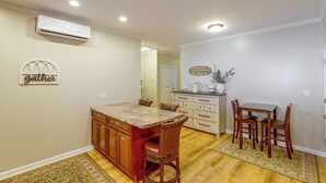 Una cocina con comedor, armarios de madera, encimera de mármol y aire acondicionado instalado en la pared.