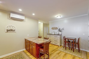 Una cocina con comedor, armarios de madera, encimera de mármol y aire acondicionado instalado en la pared.
