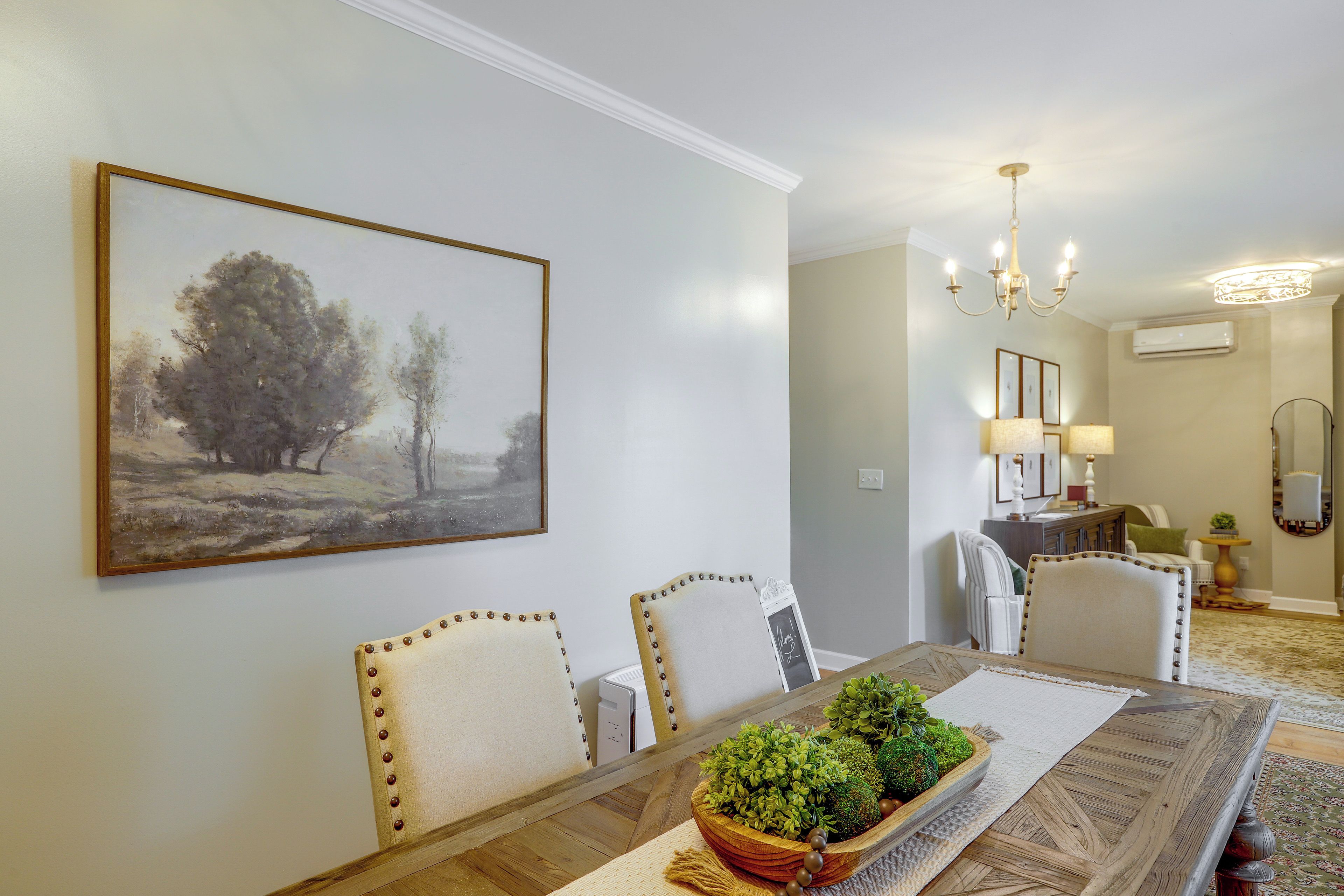 A dining area with a table, chairs, a chandelier, and a painting on the wall.