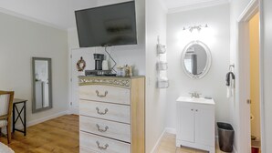 Un dormitorio con una televisión montada sobre un tocador, un espejo sobre el lavabo y una puerta que da a otra habitación.