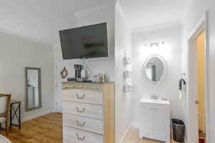 Un dormitorio con una televisión montada sobre un tocador, un espejo sobre el lavabo y una puerta que da a otra habitación.