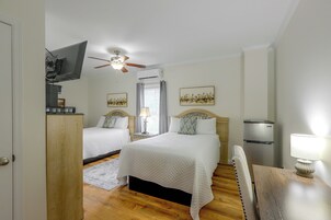 Habitación de hotel con dos camas, ventilador de techo, aire acondicionado, televisor y obras de arte en las paredes.