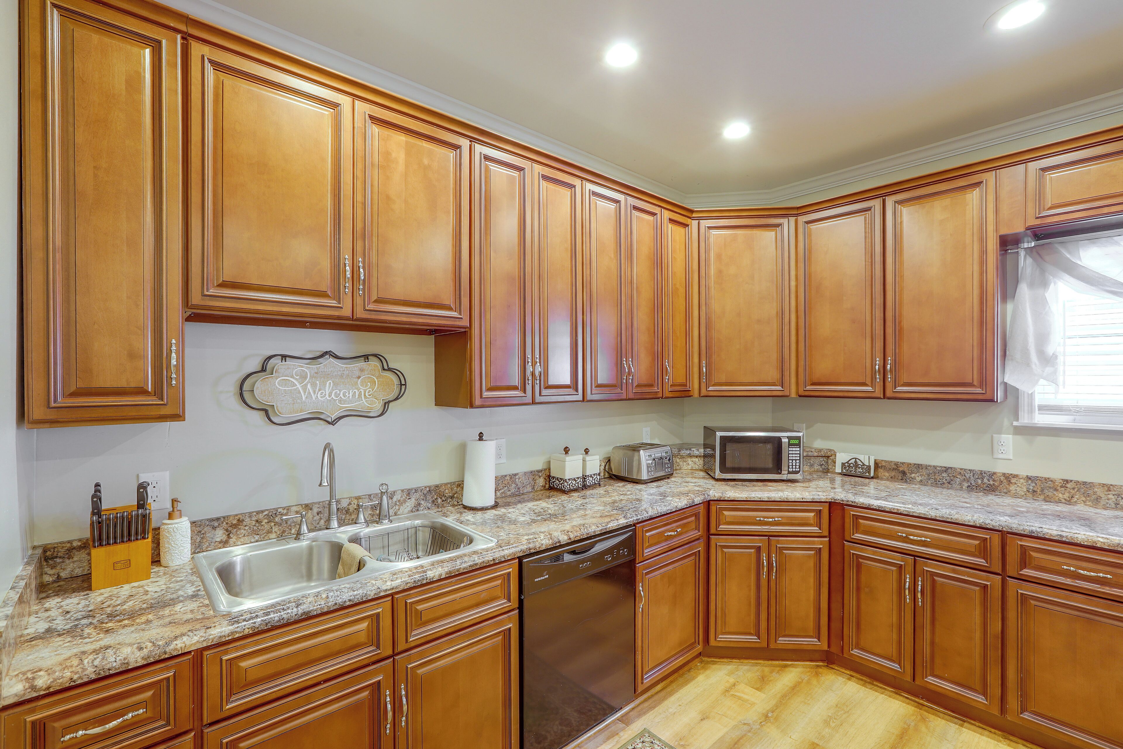 A kitchen with wooden cabinets, a granite countertop, a stainless steel sink, a dishwasher, a toaster, and a microwave.