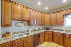 Una cocina con armarios de madera, encimera de granito, pileta de acero inoxidable, lavavajillas, tostadora y microondas.
