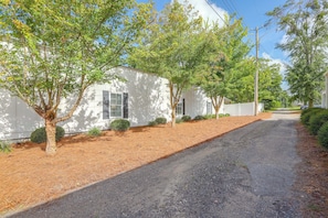 A residential street with white houses, a gravel driveway, and trees.