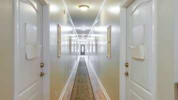 Un pasillo de hotel con puertas blancas, alfombra estampada y una lámpara en el techo.