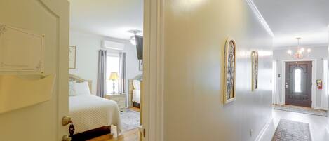 Un pasillo de hotel con una cama, una mesita de noche, una lámpara y una puerta que da a otra habitación.