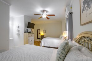A hotel room with two beds, a ceiling fan, a flat-screen TV, a desk with a lamp, and a framed picture on the wall.