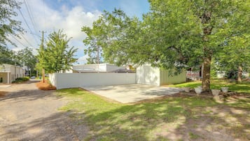A residential area with a paved driveway, a white fence, and a large tree.