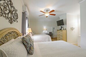 Habitación de hotel con dos camas, ventilador de techo, televisor y cómoda.