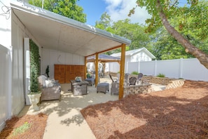 A covered patio area with outdoor furniture, a white fence, and a tree.
