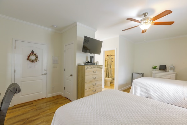 A bedroom with two beds, a ceiling fan, a television, and a dresser.