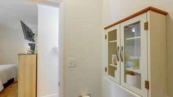 A bathroom with a toilet, a cabinet with glass doors, and a bed in the adjacent room.