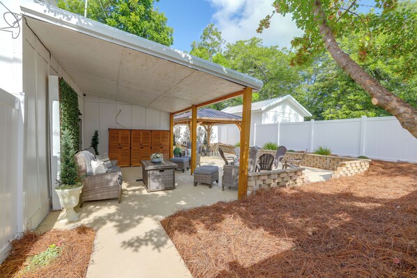 Un patio cubierto con mobiliario exterior, cerca blanca y un árbol.