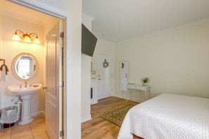 Un dormitorio con una cama, una mesita de noche con una planta, un espejo y una puerta que da a un baño con un lavabo y un inodoro.
