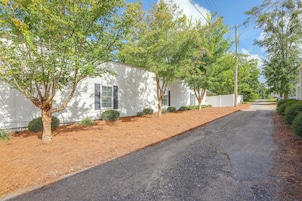 Una calle residencial con casas blancas, un camino de grava y árboles.