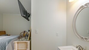 Un dormitorio con cama, mesita de noche y cómoda. Hay un espejo en la pared y una lámpara sobre la cómoda.