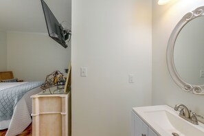 A bedroom with a bed, bedside table, and a dresser. There is a mirror on the wall and a light fixture above the dresser.
