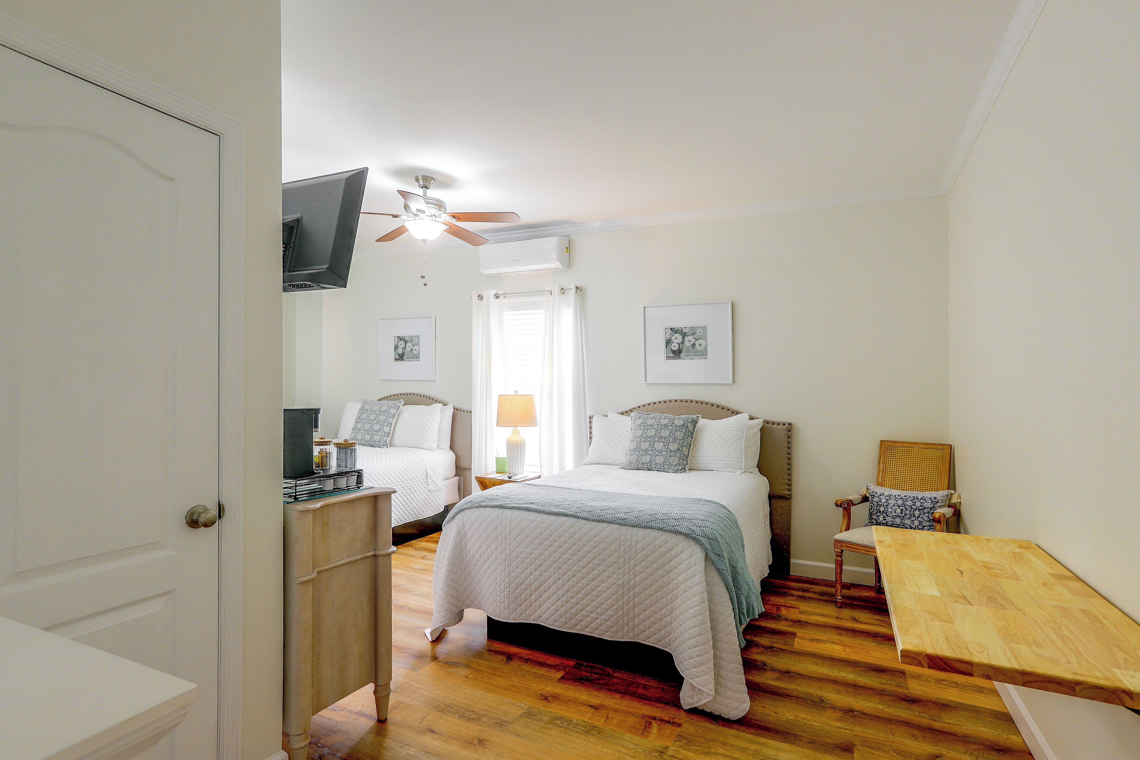 A bedroom with two beds, a ceiling fan, and a TV mounted on the wall.