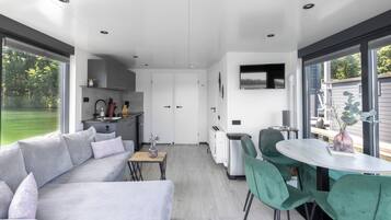 A modern kitchen with built-in appliances, a dining area with green chairs, and a large window overlooking a garden.
