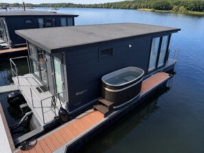 A floating houseboat with a covered deck, a hot tub, and a view of the water.